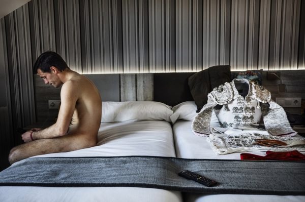 Jordi Cohen matador sitting on the bed with his clothes on the other side