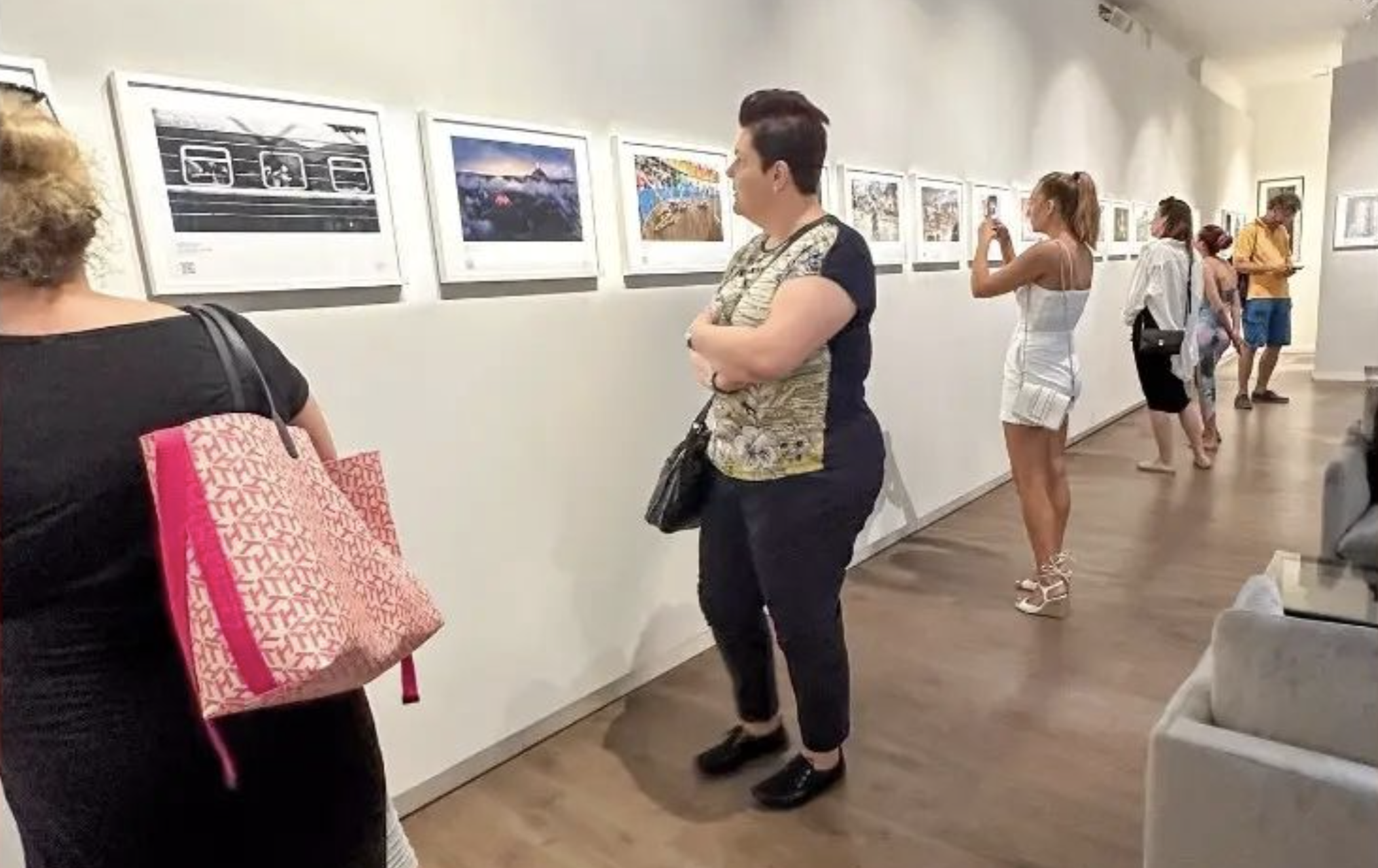 People stand and look at framed photographs on the wall.